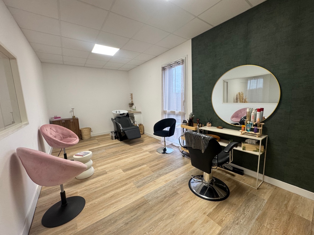 Grande salle équipée de plusieurs postes, d’un bac de lavage et d’un miroir rond