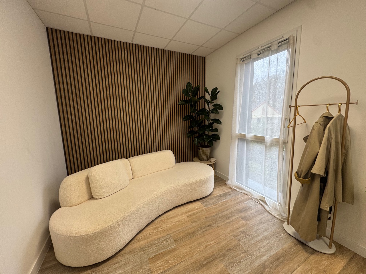 Salon avec canapé bouclé crème, mur de tasseaux bois, plante et portant