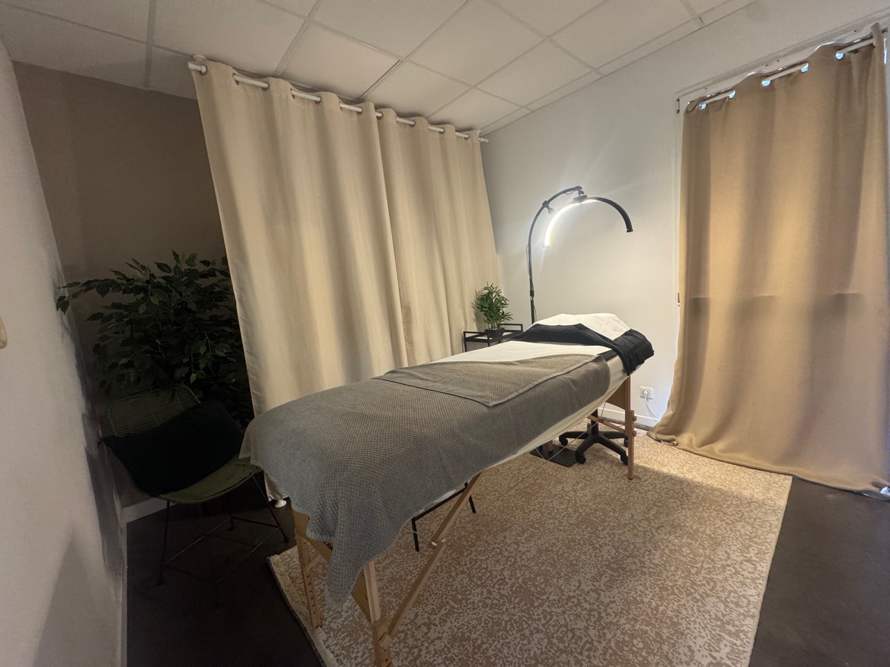 Salle tamisée avec table de massage, rideaux clairs et plantes